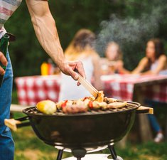 man-cooking-meat-on-barbecue-chef-putting-some-sausages-on-grill-in-park-outdoor